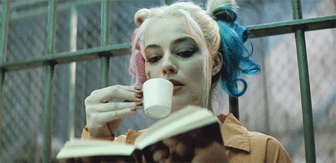 Gif da personagem Harley Quinn lendo um livro e tomando um café.
